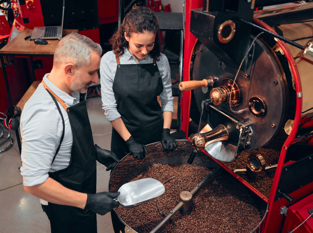 two individuals next to a machine of coffee beans